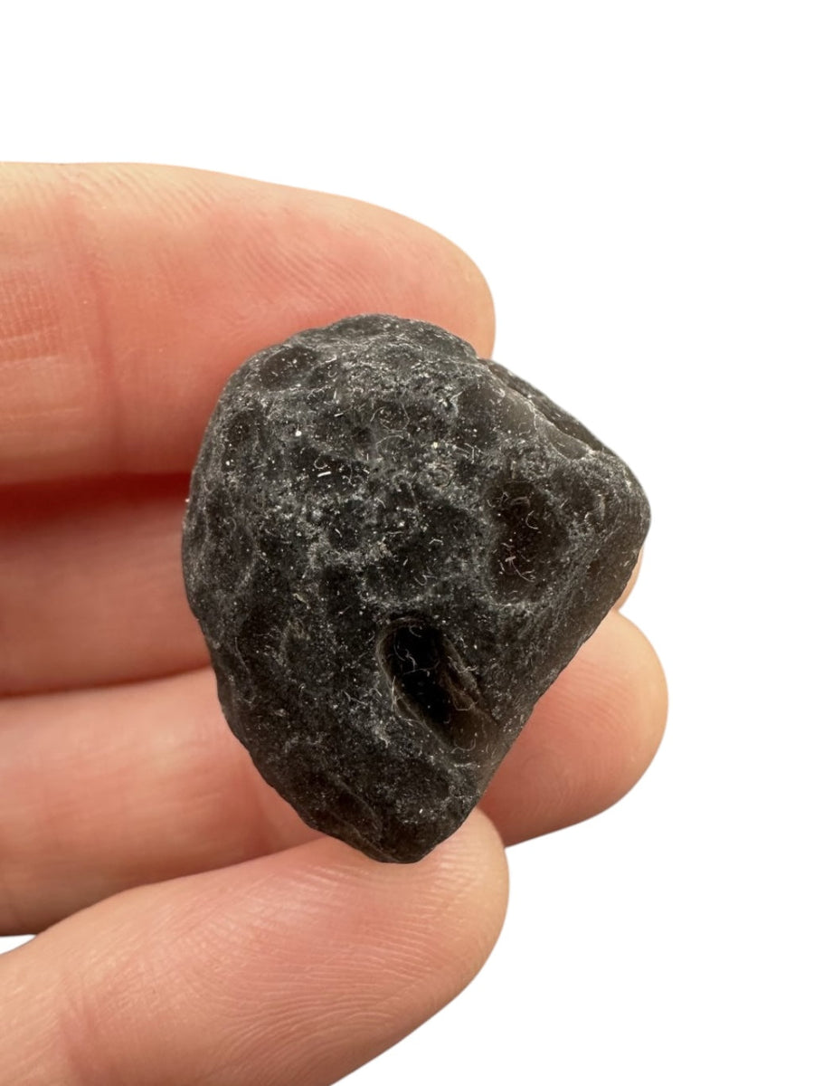 Saffordite grezza grigio-nera opaca con superficie butterata da profonde cavità tondeggianti