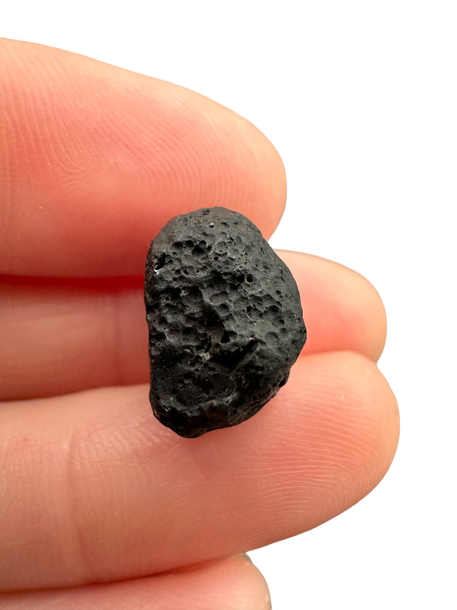 Belizeite grezza nera con superficie scavata da cavità tondeggianti e solchi profondi