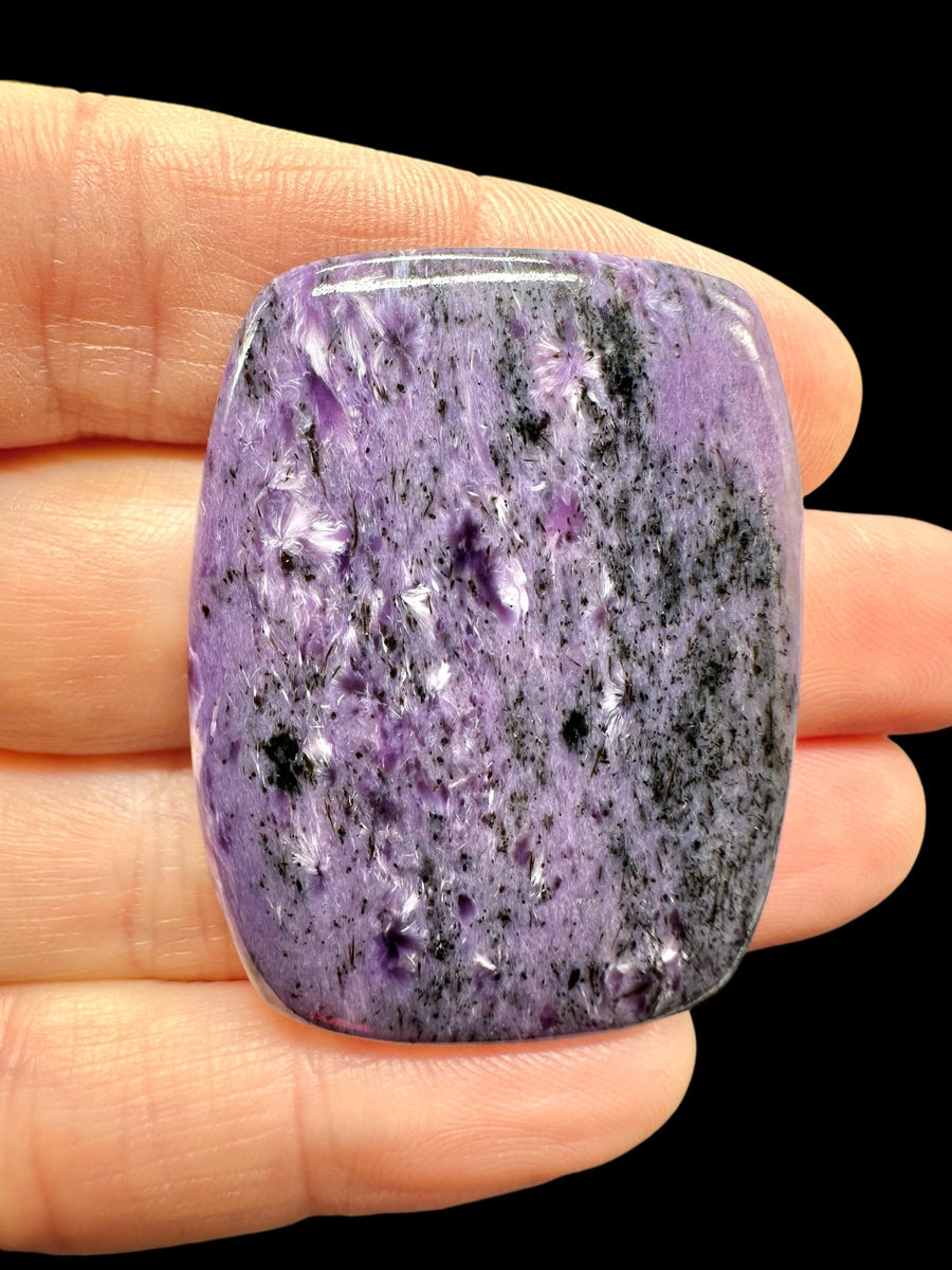 Cabochon rettangolare di charoite viola con ciuffi fibrosi bianchi e screziature nere