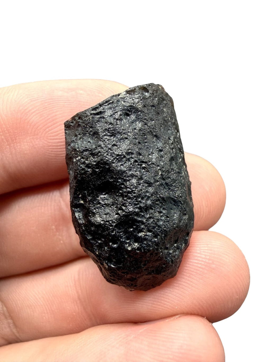 Geriasite grezza nera allungata con superficie butterata e riflessi verde scuro