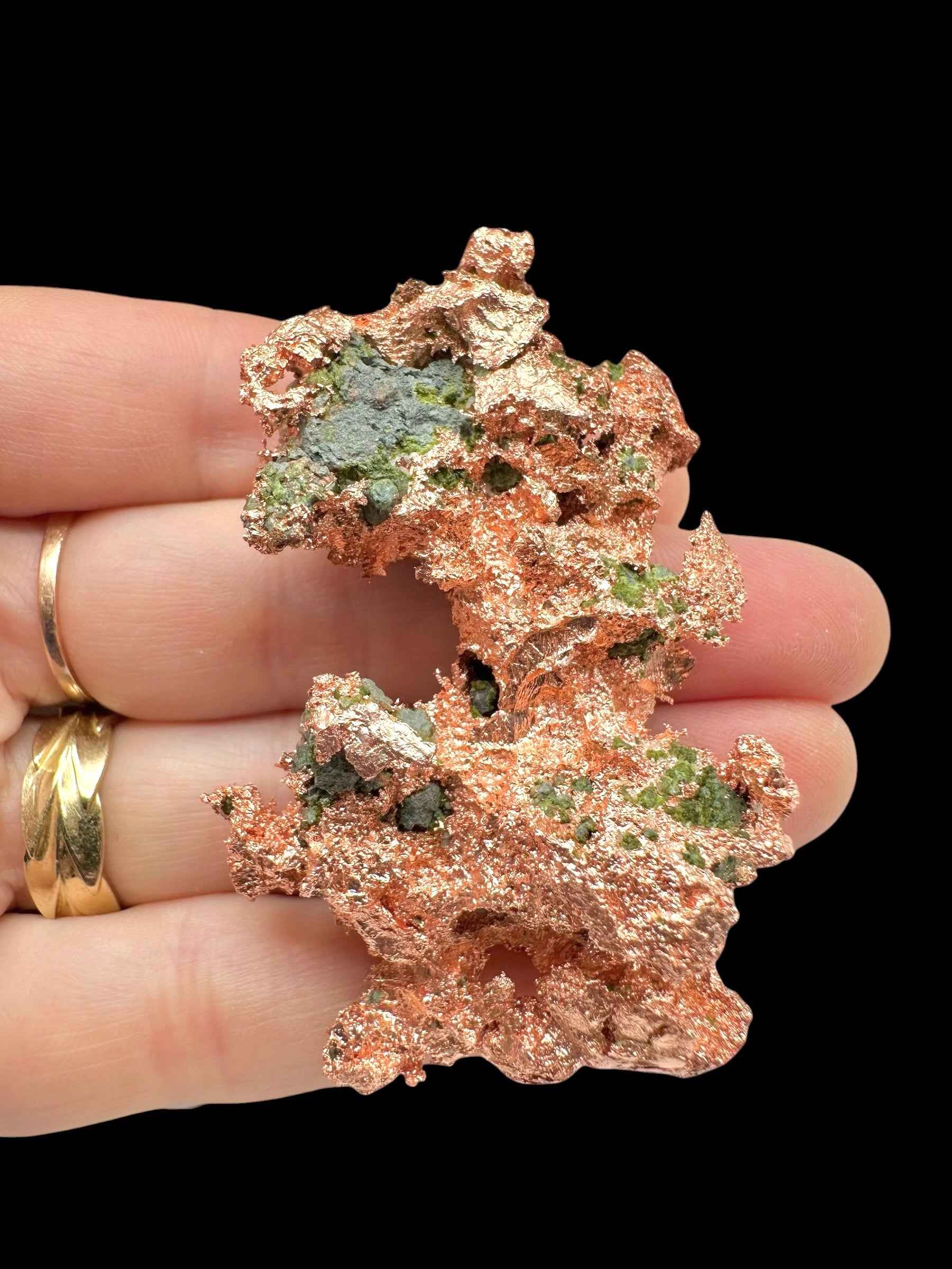Lamina di rame nativo del Michigan con chiazze verdi di malachite, tenuta tra le dita su fondo nero