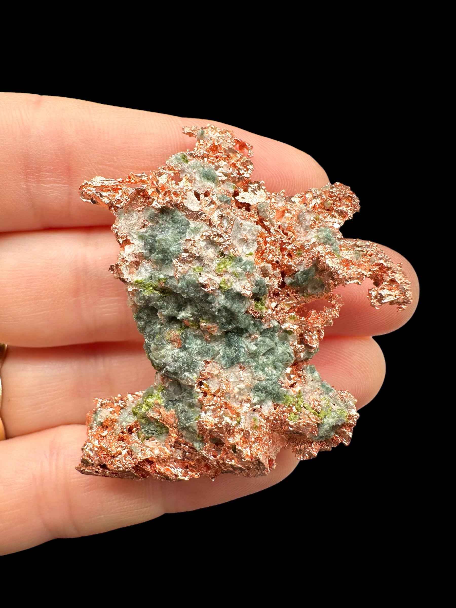 Placca di rame nativo del Michigan con masse di malachite verde-grigio al centro, tenuta fra le dita