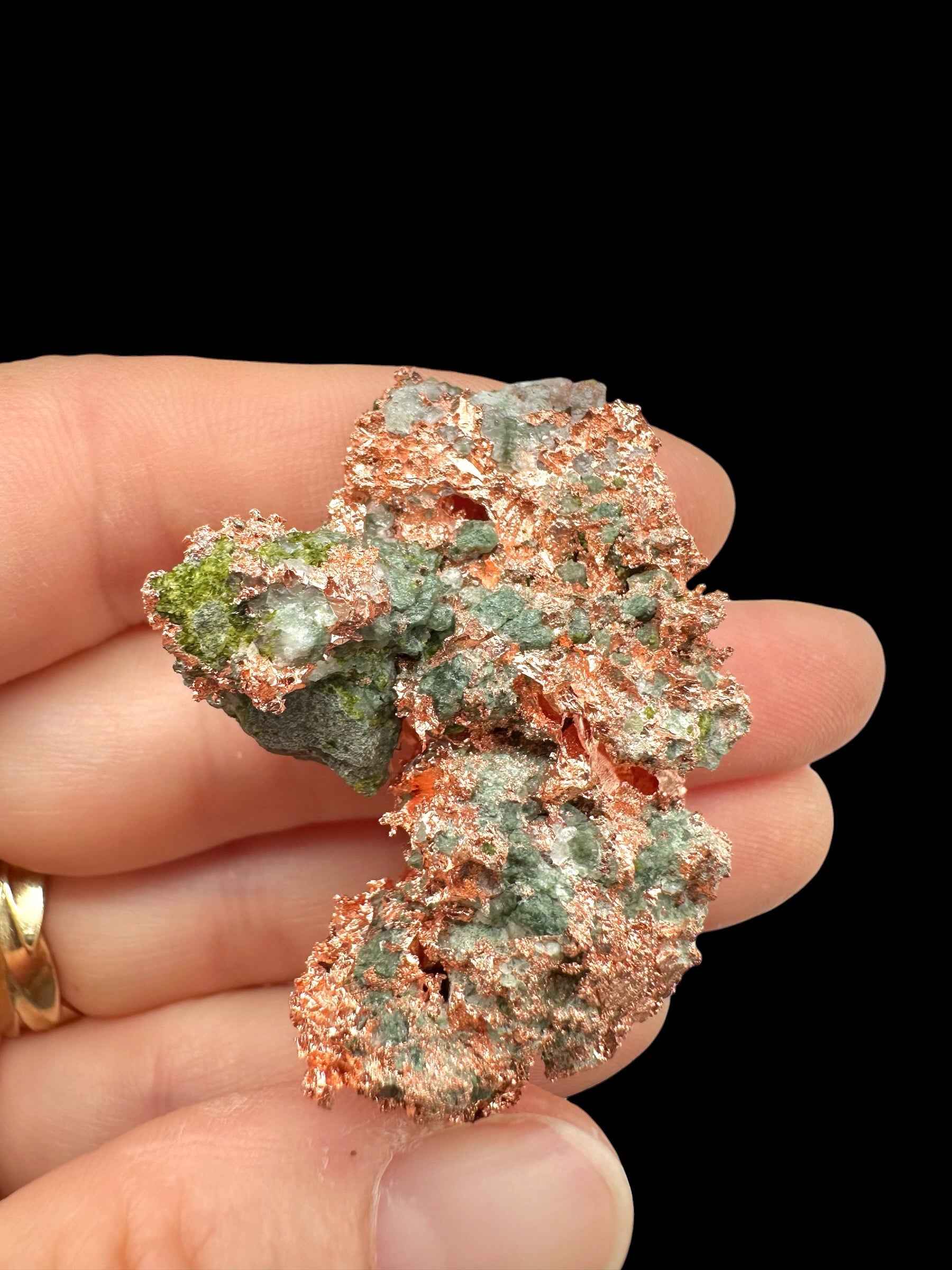 Esemplare di rame nativo con malachite verde dal Michigan tenuto tra le dita, lamelle metalliche rosa-arancio