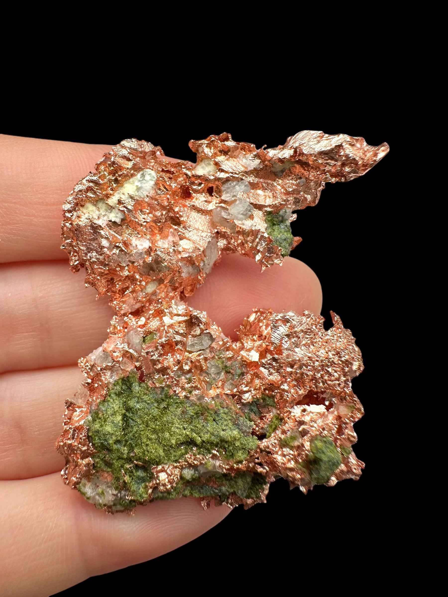 Campione di rame nativo del Michigan con lamelle metalliche ramate e chiazze verdi di malachite, tenuto tra le dita