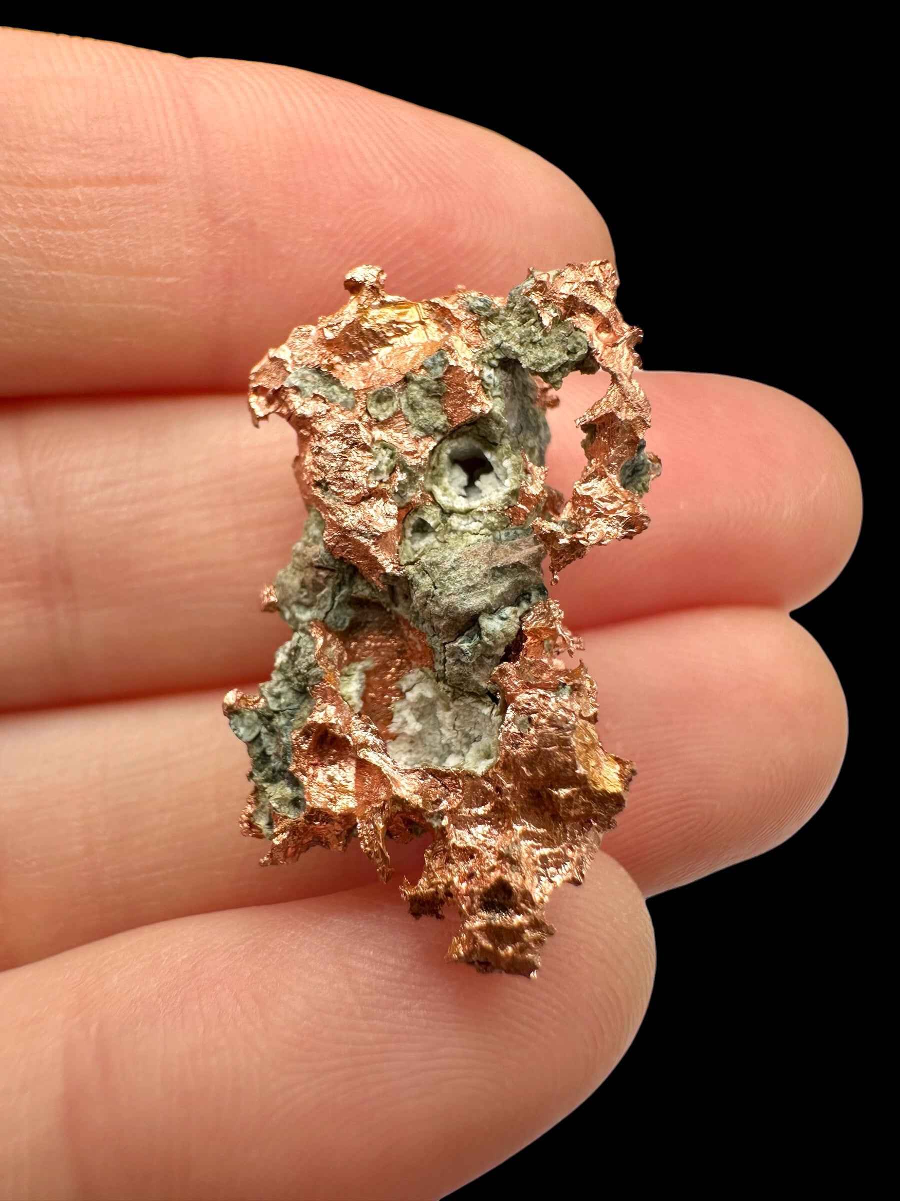 Lamina di rame nativo del Michigan con patine verdi di malachite e bordi frangiati, tenuta fra le dita