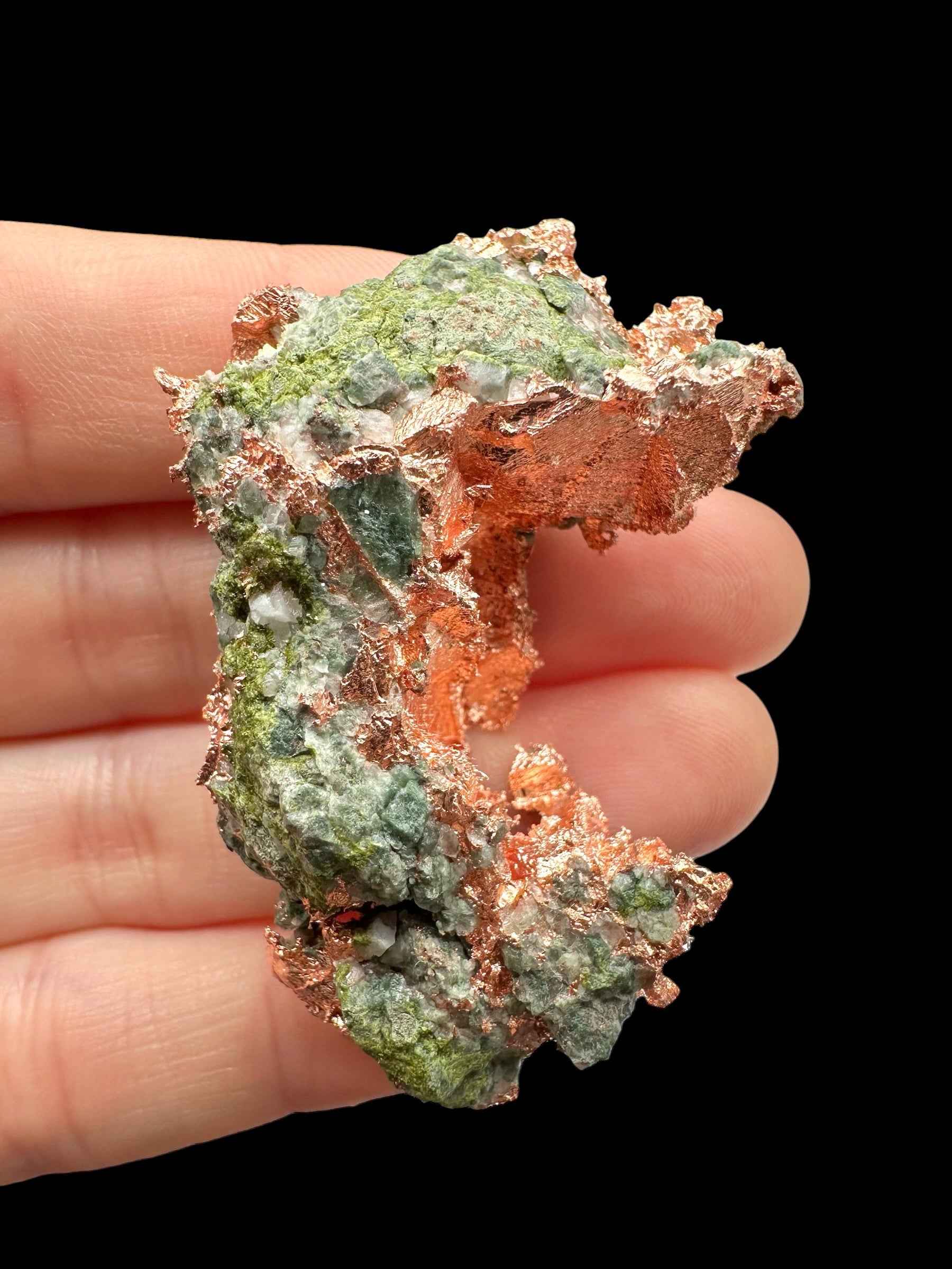Campione di rame nativo con malachite verde dal Michigan, tenuto tra le dita su fondo nero