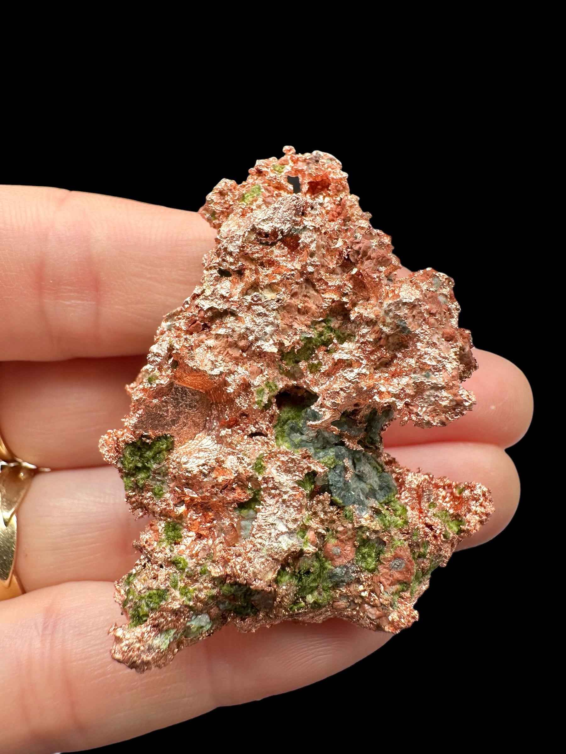 Rame nativo del Michigan con macchie di malachite verde, superficie granulosa e riflessi ramati, tenuto in mano