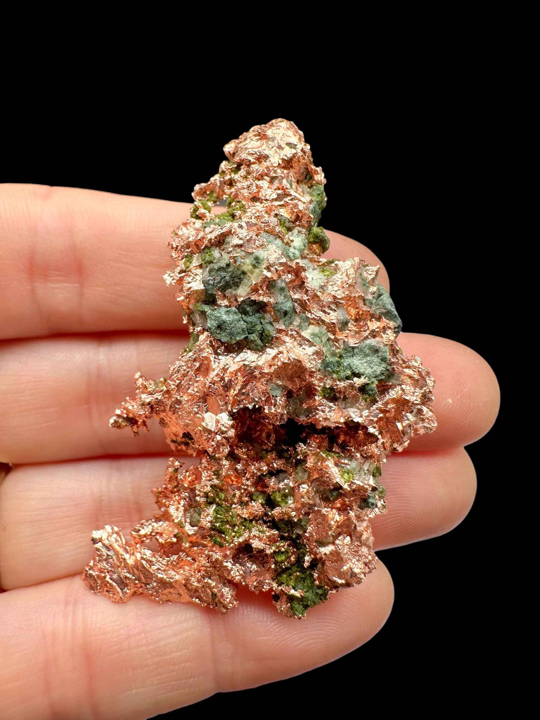 Lamina di rame nativo del Michigan tenuta in mano, con chiazze verdi di malachite nelle cavità