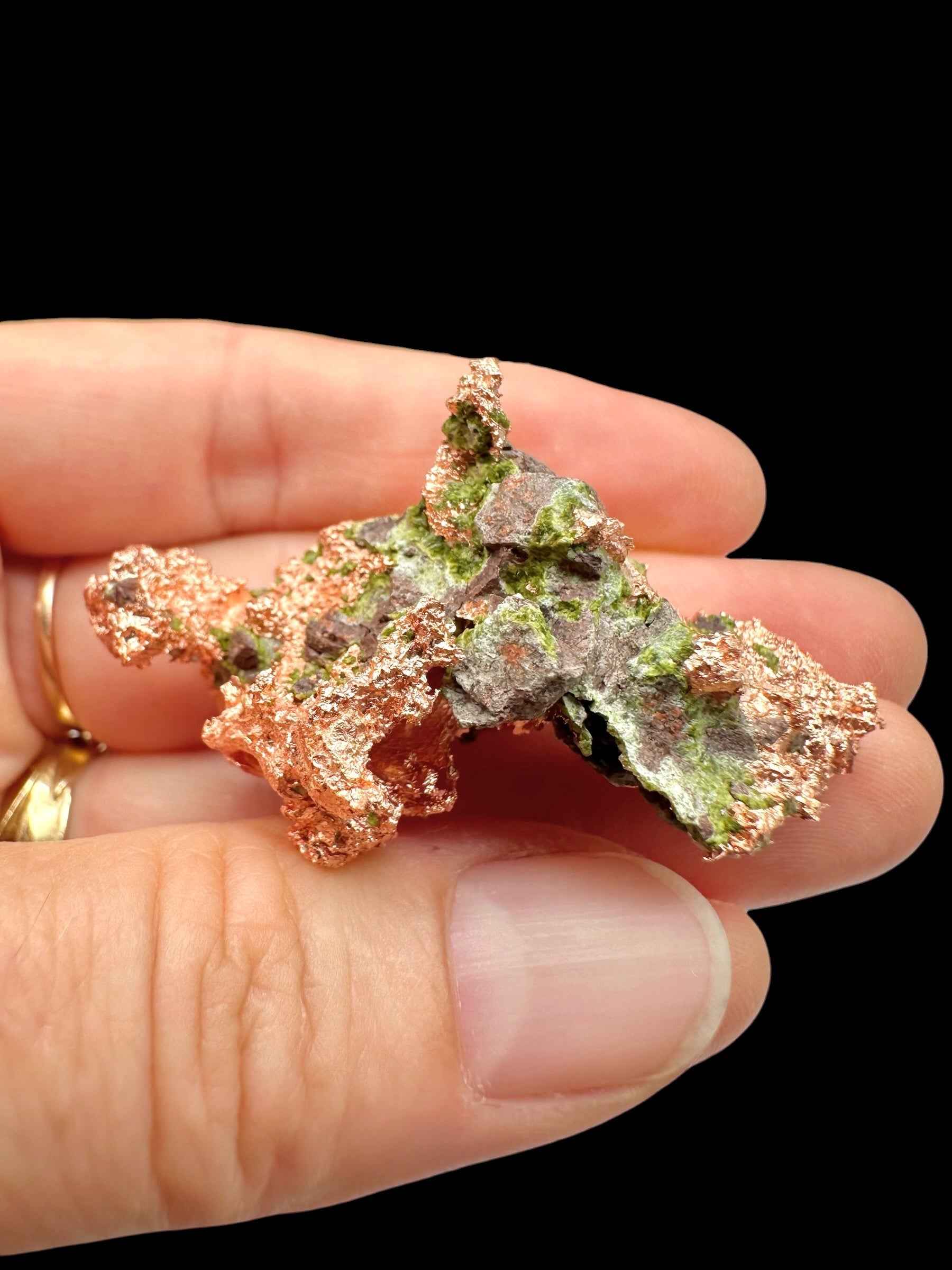 Esemplare di rame nativo del Michigan con chiazze di malachite verde, tenuto tra le dita