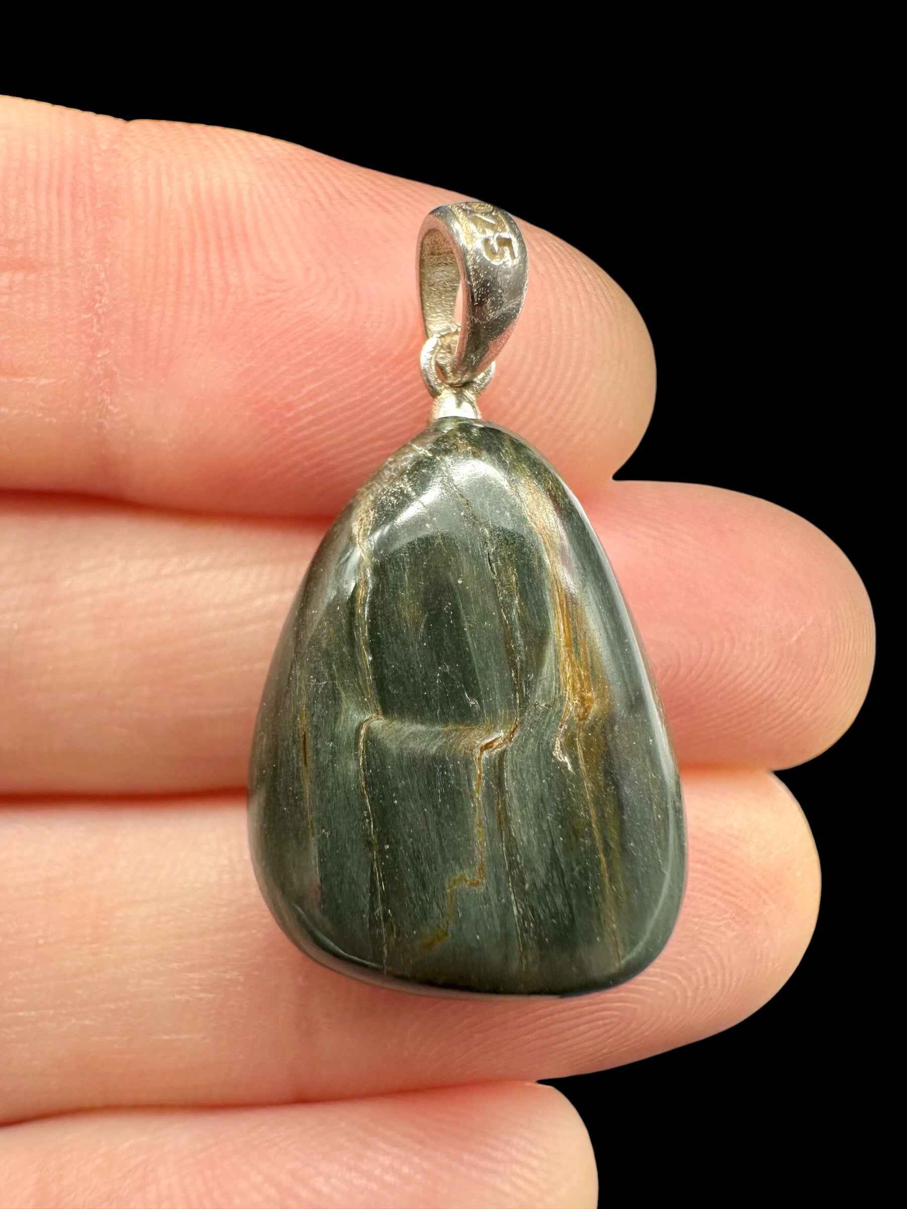 Pendente in occhio di gatto verde scuro con venature ocra, montatura in argento, tenuto tra le dita