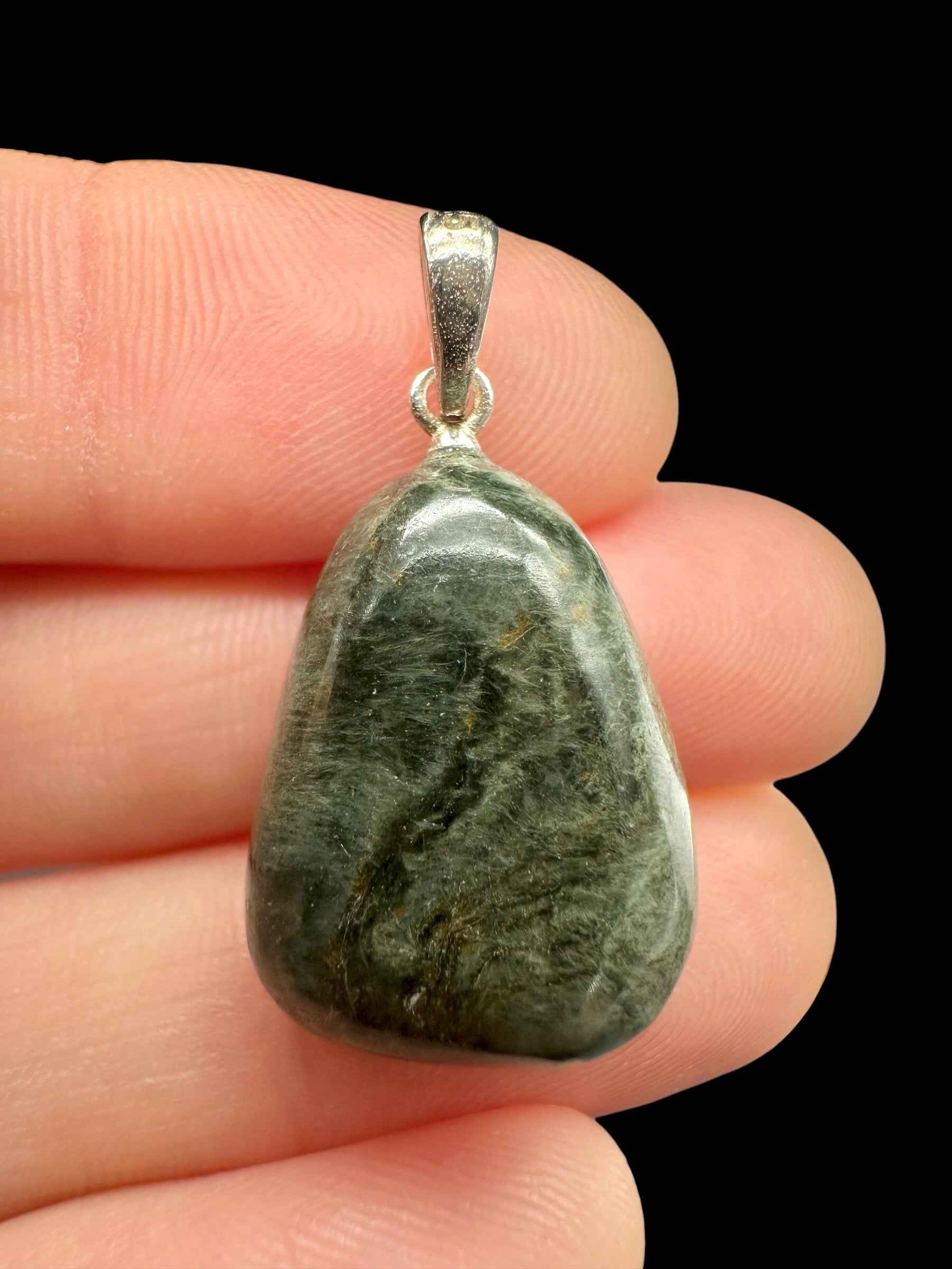 Pendente in occhio di gatto verde scuro di forma triangolare arrotondata con appiccagnolo in argento, tenuto tra le dita