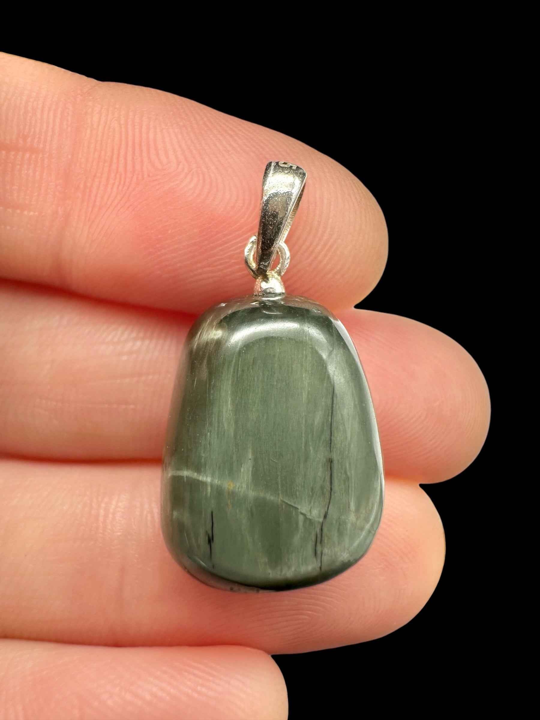 Pendente in occhio di gatto verde grigio burattato con appiccagnolo in argento, tenuto tra le dita