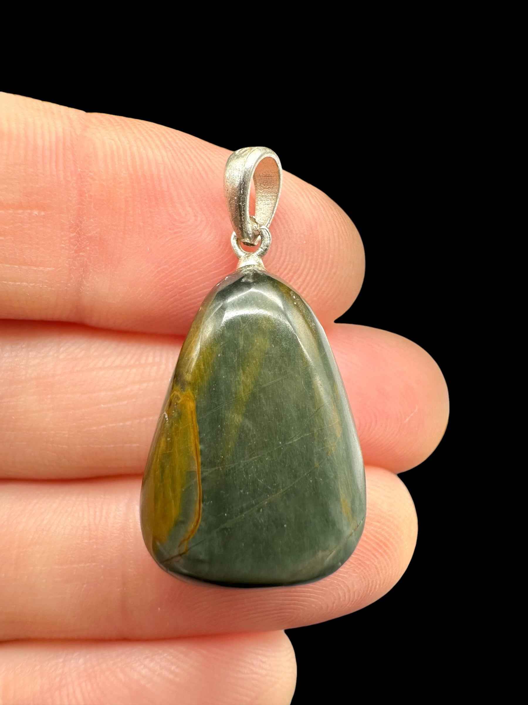 Pendente in occhio di gatto verde con vene ocra, forma a goccia levigata, cappellotto in argento, tenuto tra le dita