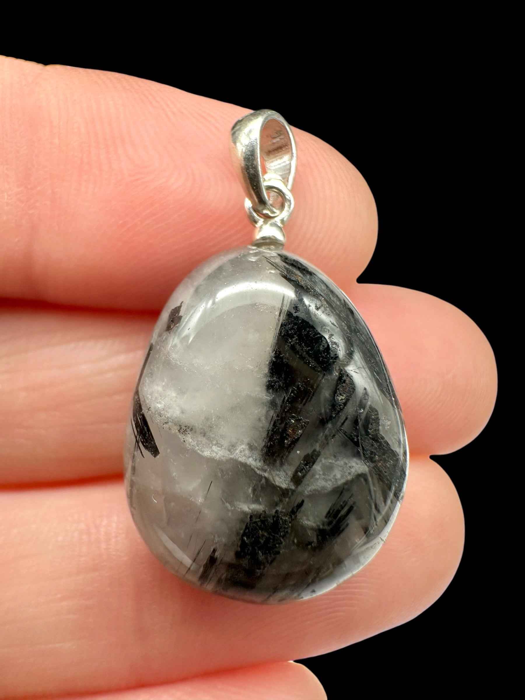 Pendente in argento con quarzo a goccia trasparente attraversato da aghi e prismi di tormalina nera, tenuto tra le dita