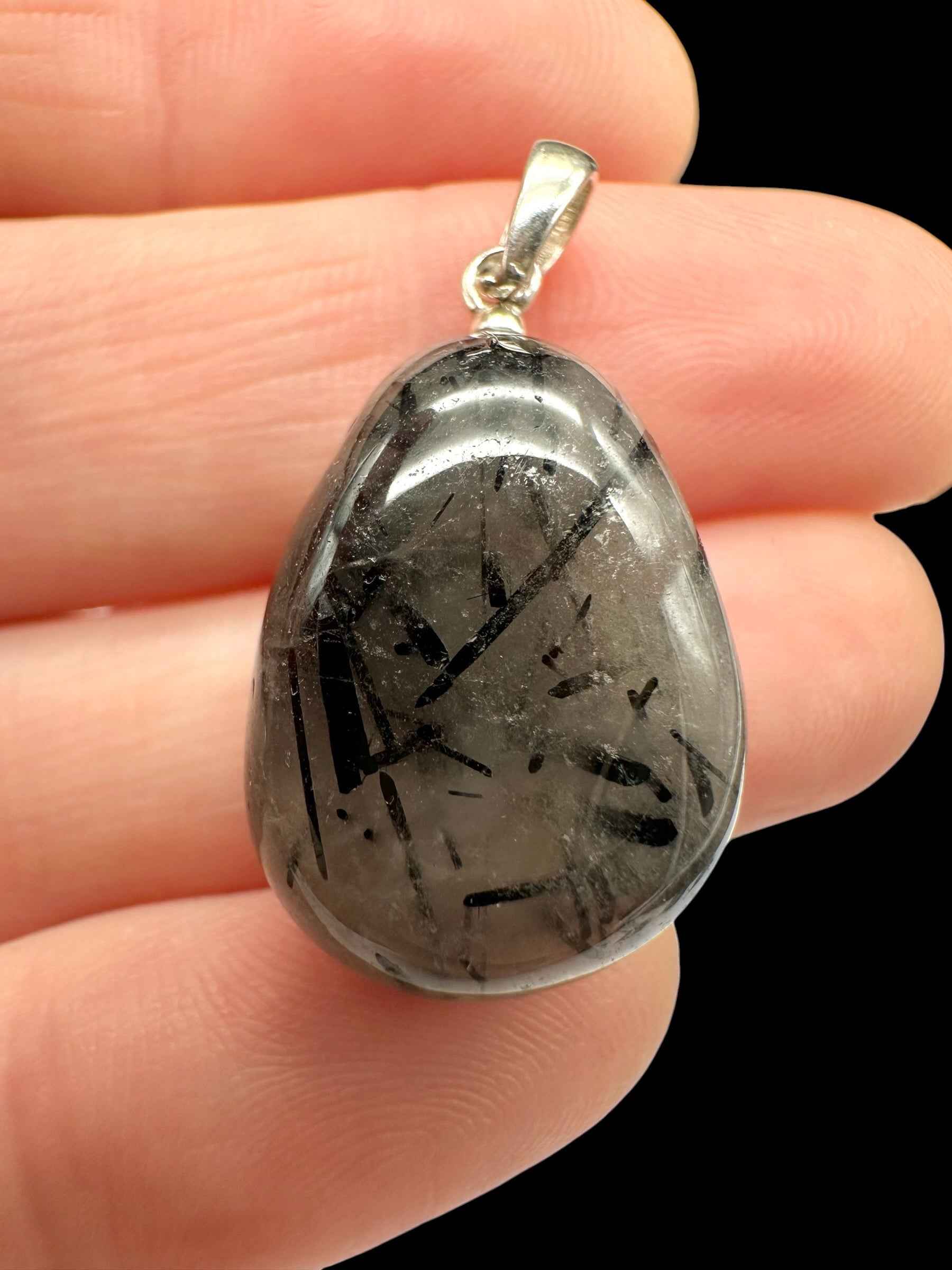 Pendente in tormalina inclusa nel quarzo, goccia lucida con aghi neri e cappuccio in argento, tenuto tra le dita
