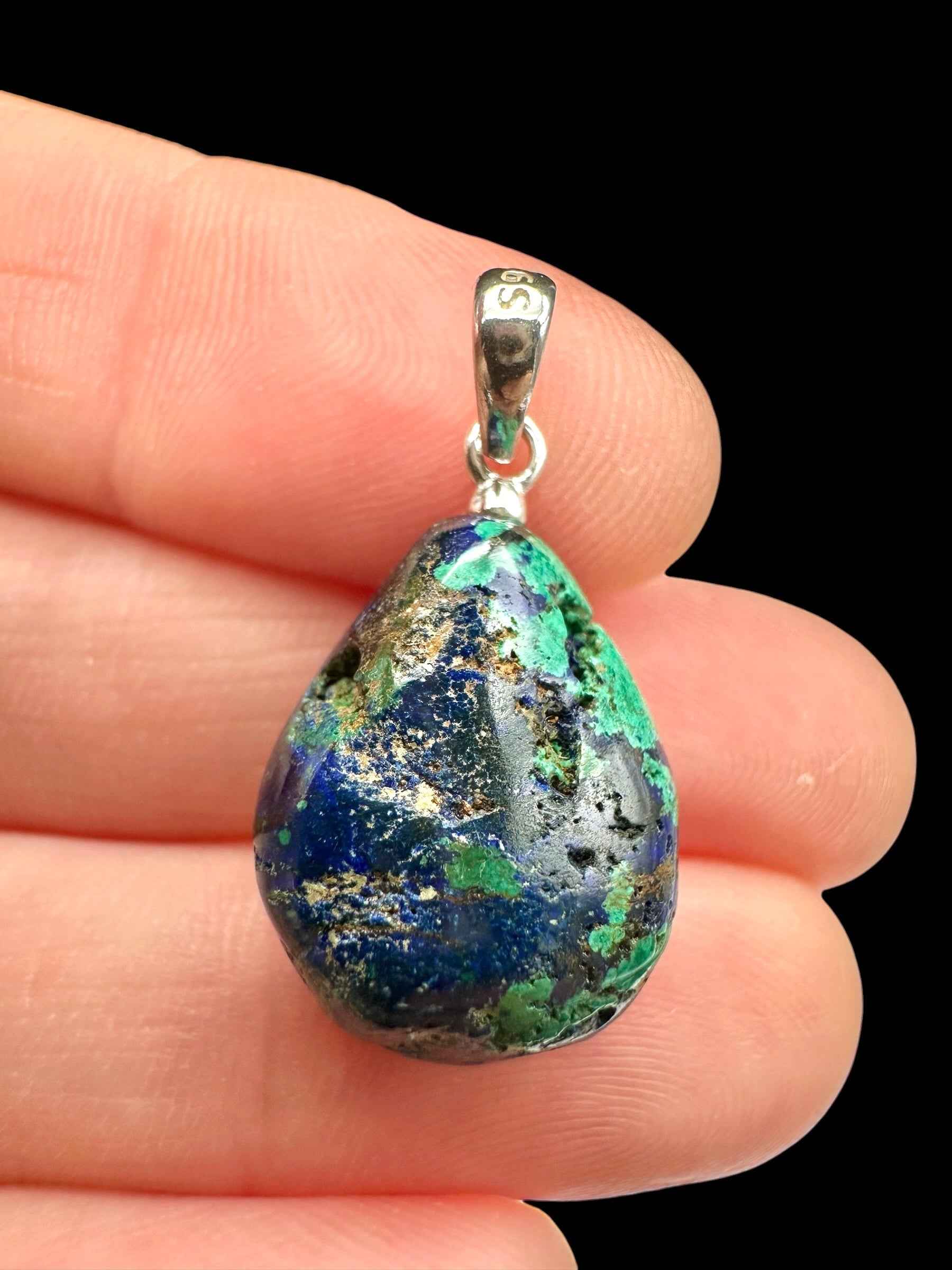 Pendente a goccia in azurite blu con macchie di malachite verde e cappuccio in argento, tenuto tra le dita