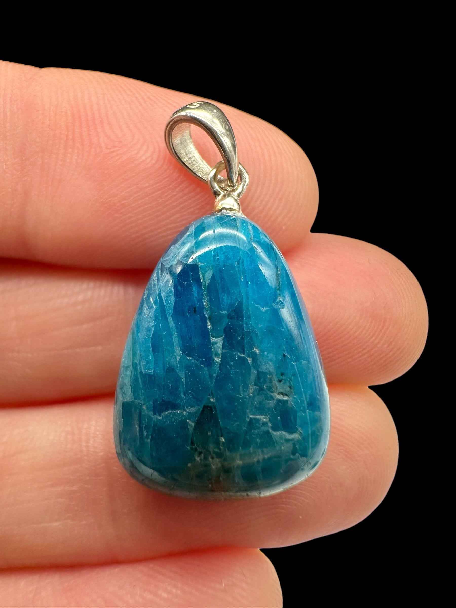 Pendente in apatite blu a forma di goccia lucidata con cappuccio e maglia in argento, tenuto tra le dita