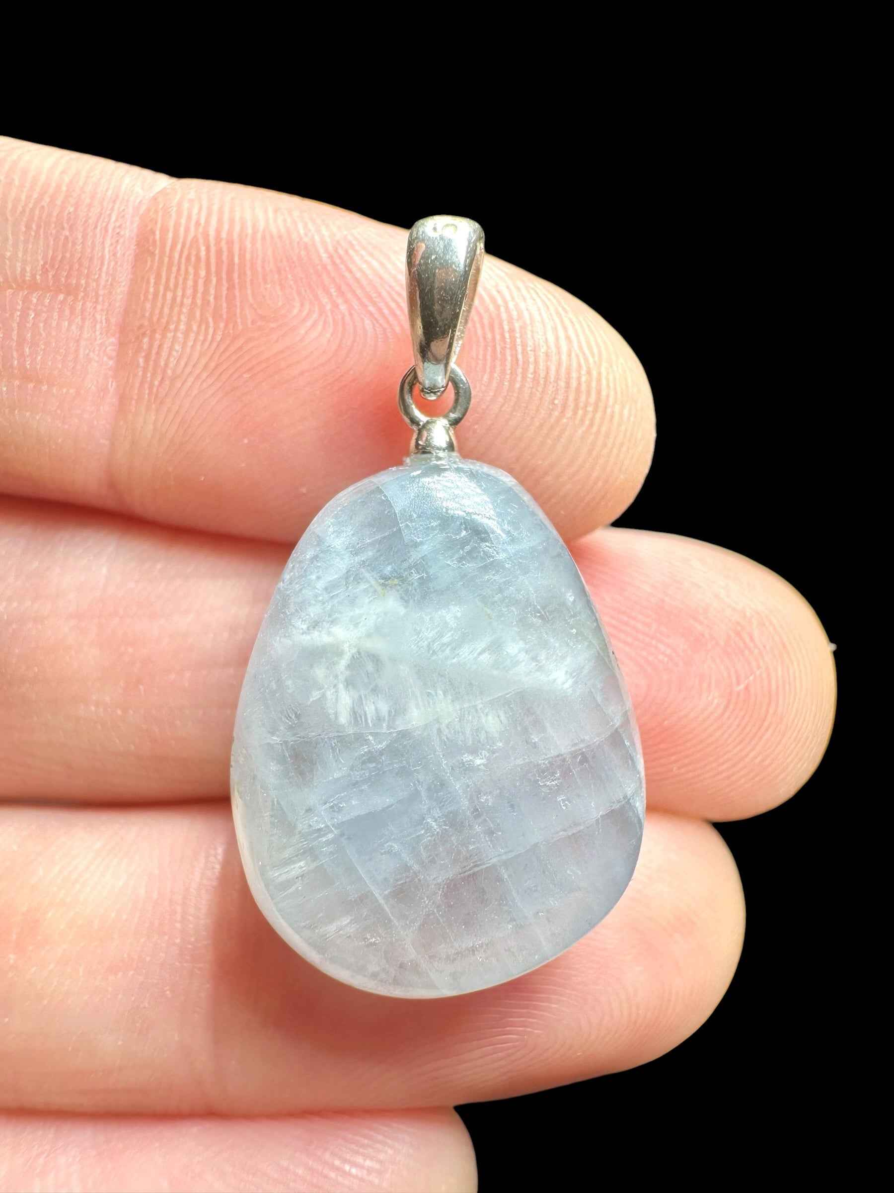 Pendente in celestite a goccia levigata azzurro pallido con montatura e appiccagnolo in argento, tenuto tra le dita