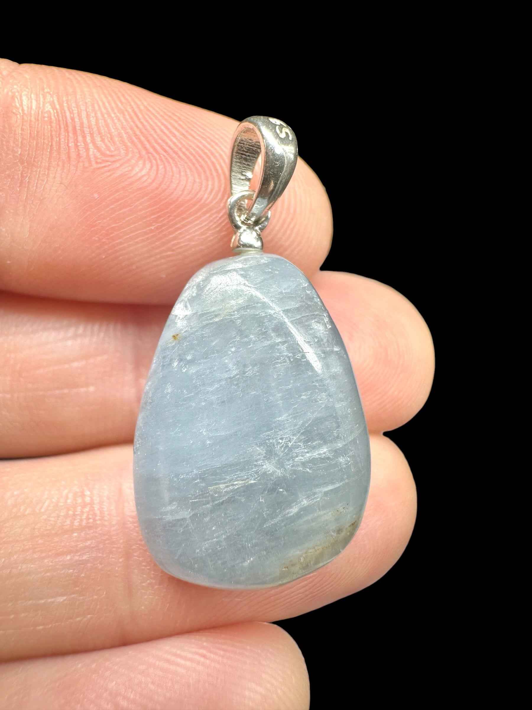 Pendente in celestite azzurra a goccia burattata con cappuccio e asola in argento, tenuto tra le dita