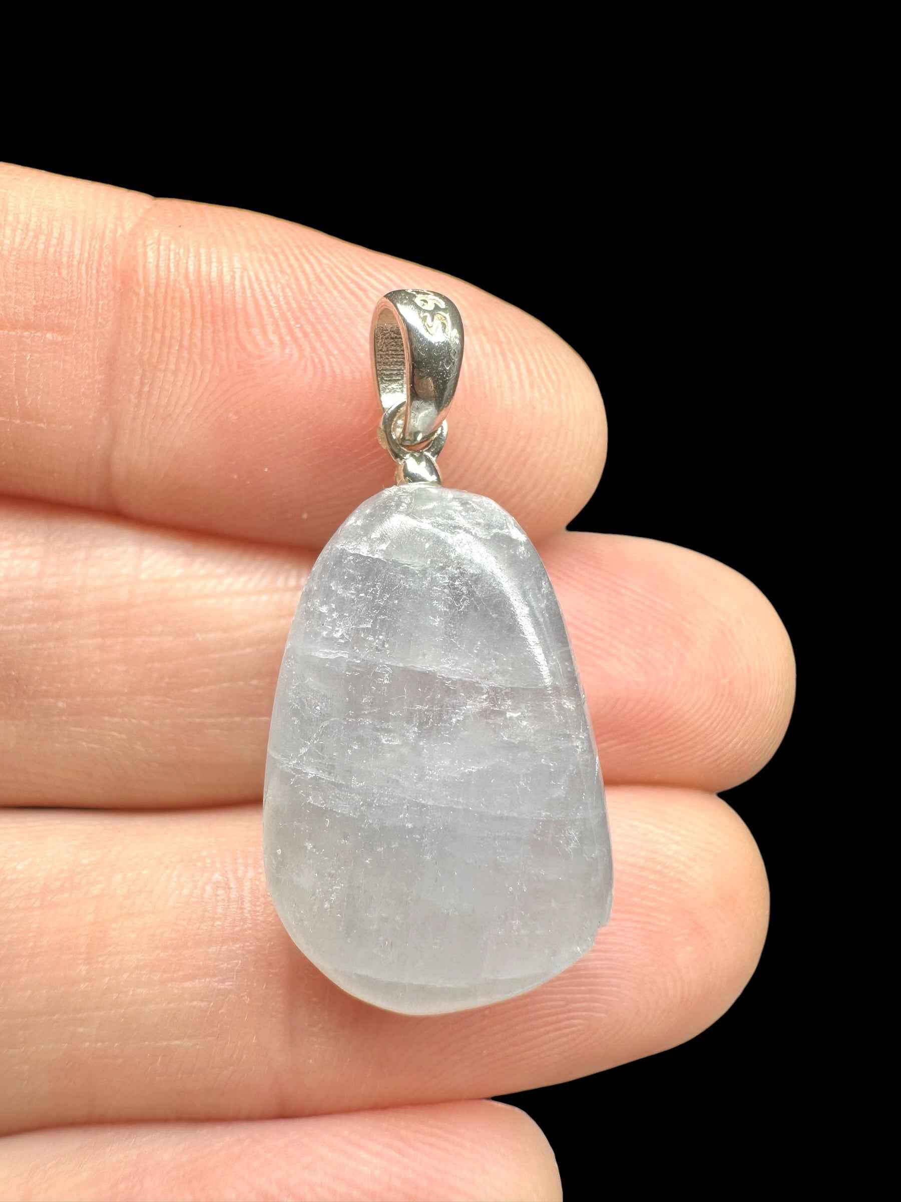 Pendente in celestite a goccia burattata, bianco traslucido, con cappuccio e ansa in argento 925, tenuto tra le dita