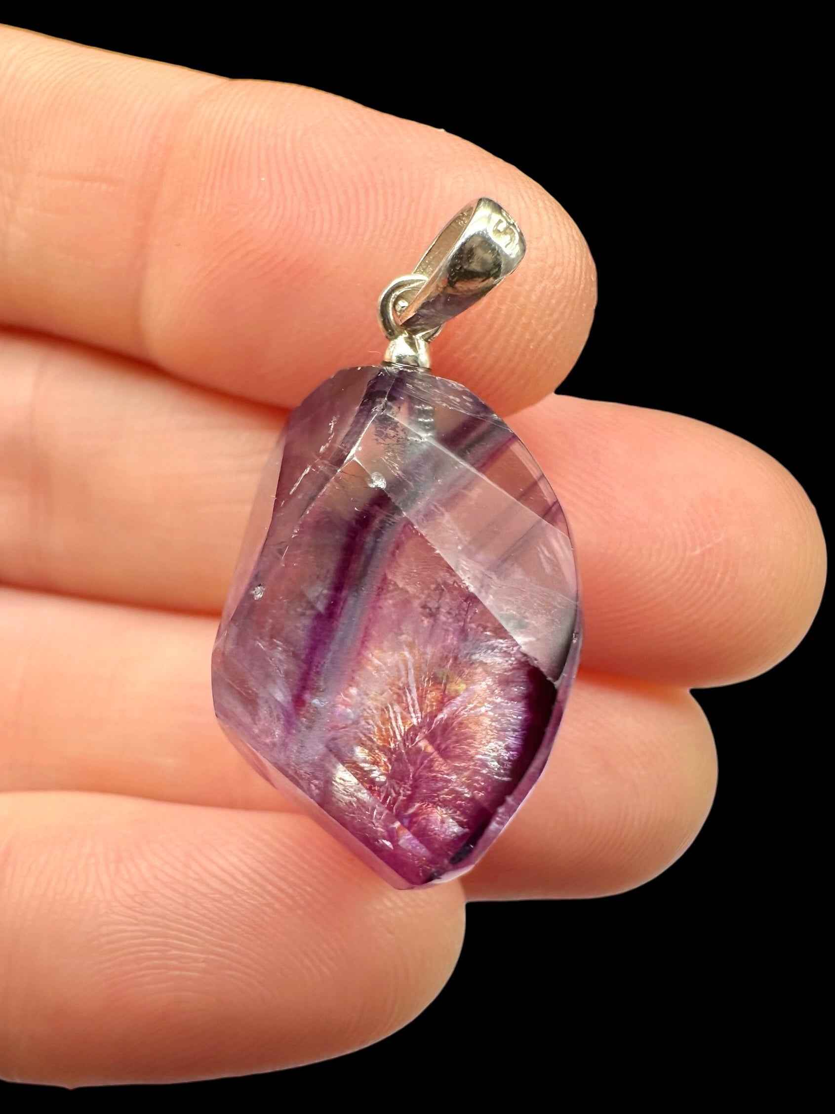 Pendente in fluorite faccettata viola e lilla con appiccagnolo in argento, tenuto tra le dita