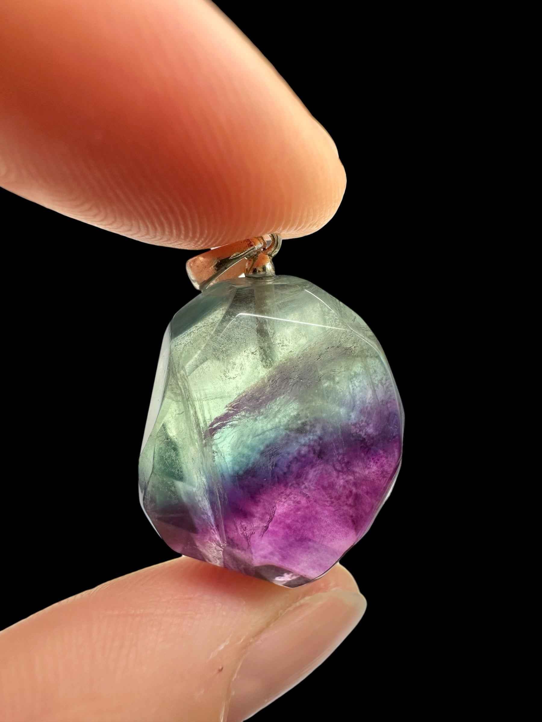 Pendente in fluorite faccettata verde e viola con cappuccio in argento, tenuto tra due dita su fondo nero