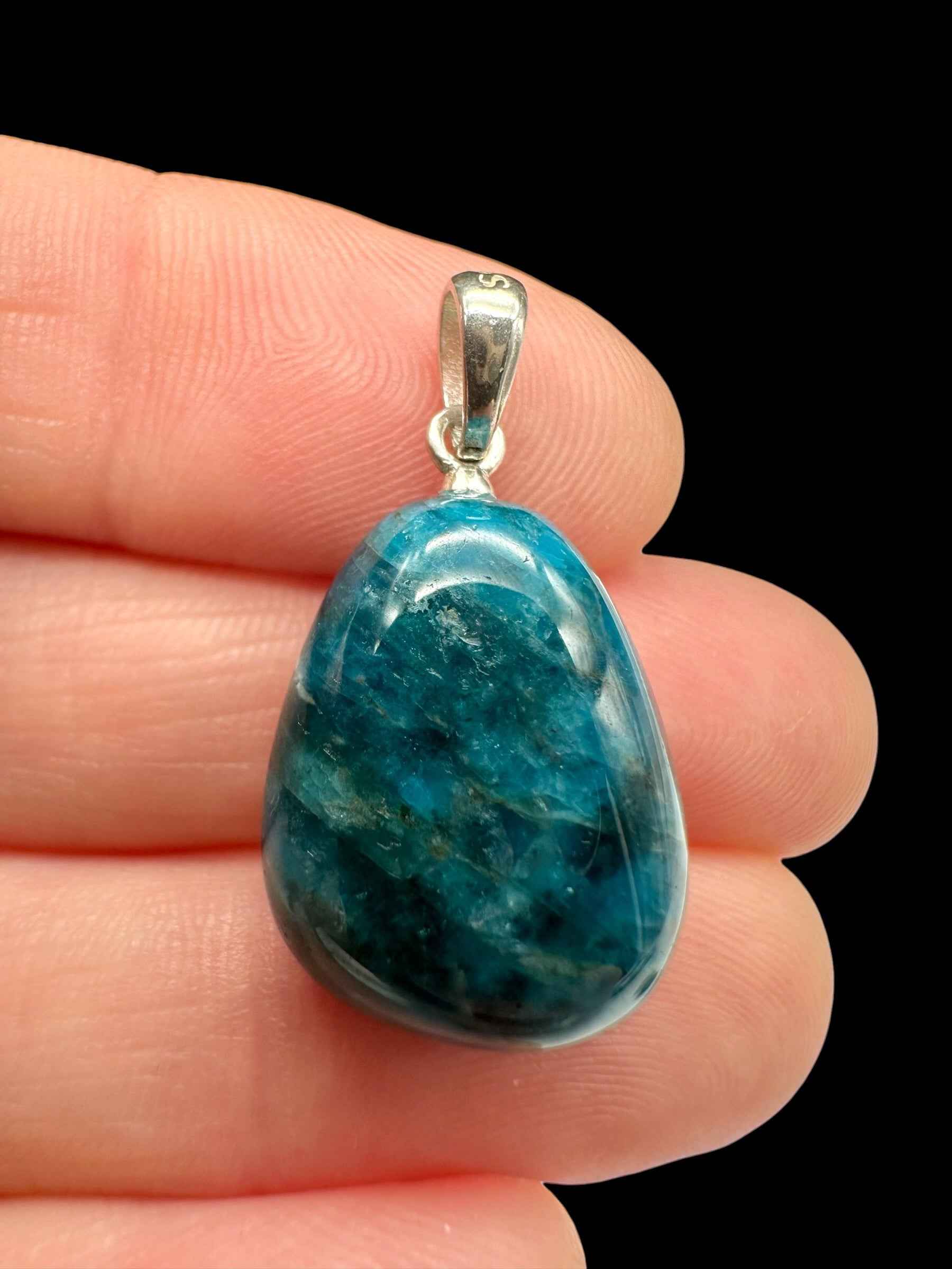 Pendente in apatite a goccia blu-verde con venature chiare, cappuccio in argento, tenuto tra le dita