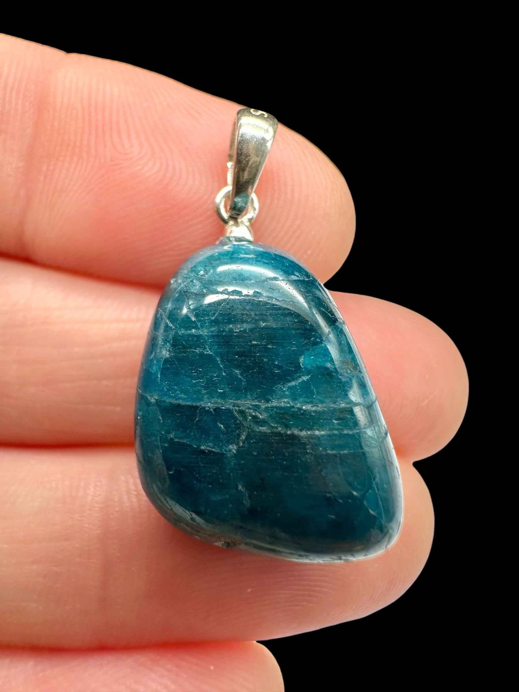 Pendente in apatite blu verdastro burattata con venature bianche e appiccagnolo in argento, tenuto tra le dita