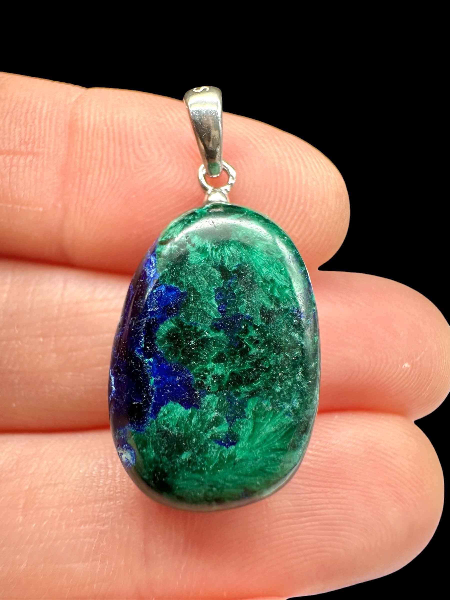 Pendente ovale in azurite e malachite verde e blu con bail in argento, tenuto tra le dita