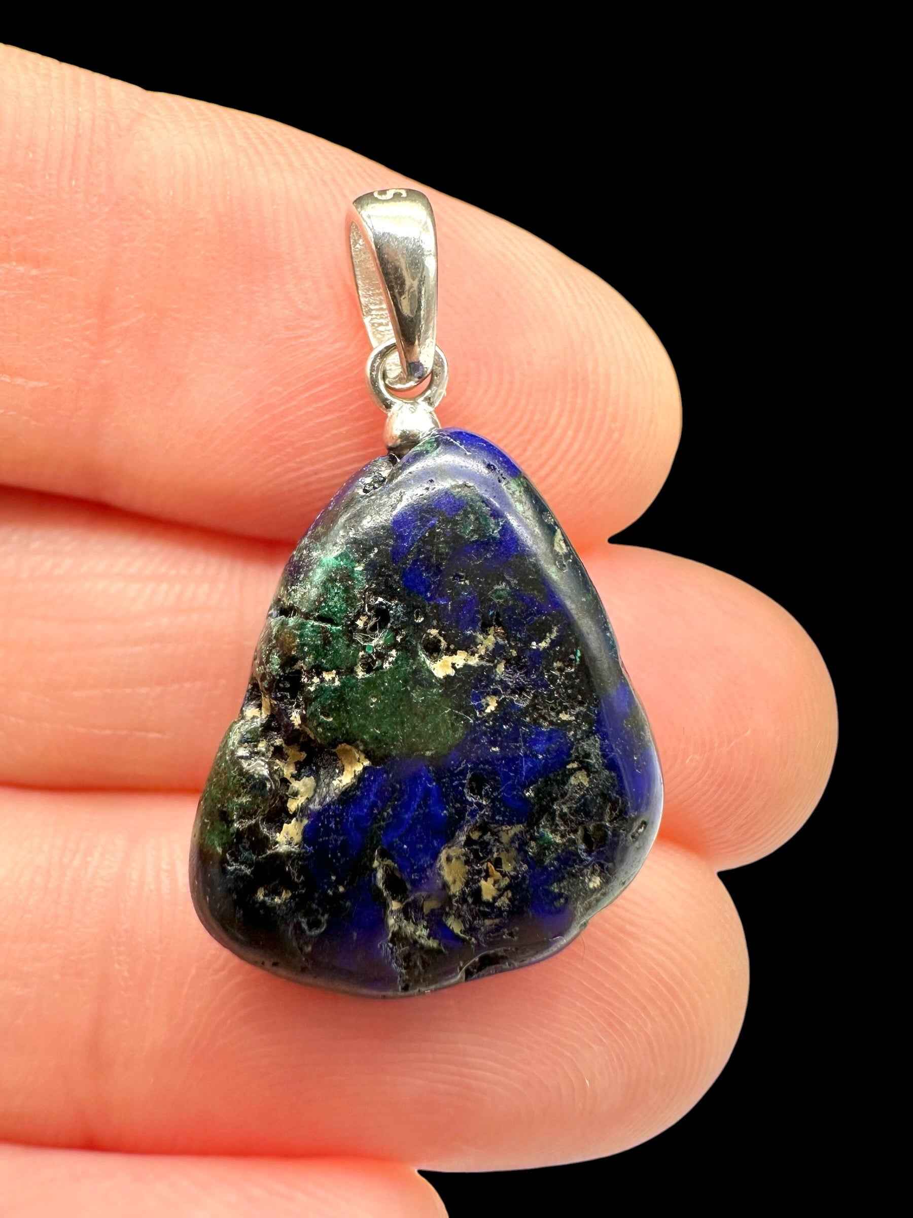 Pendente triangolare in azurite blu con chiazze di malachite verde e appiglio in argento, tenuto tra le dita