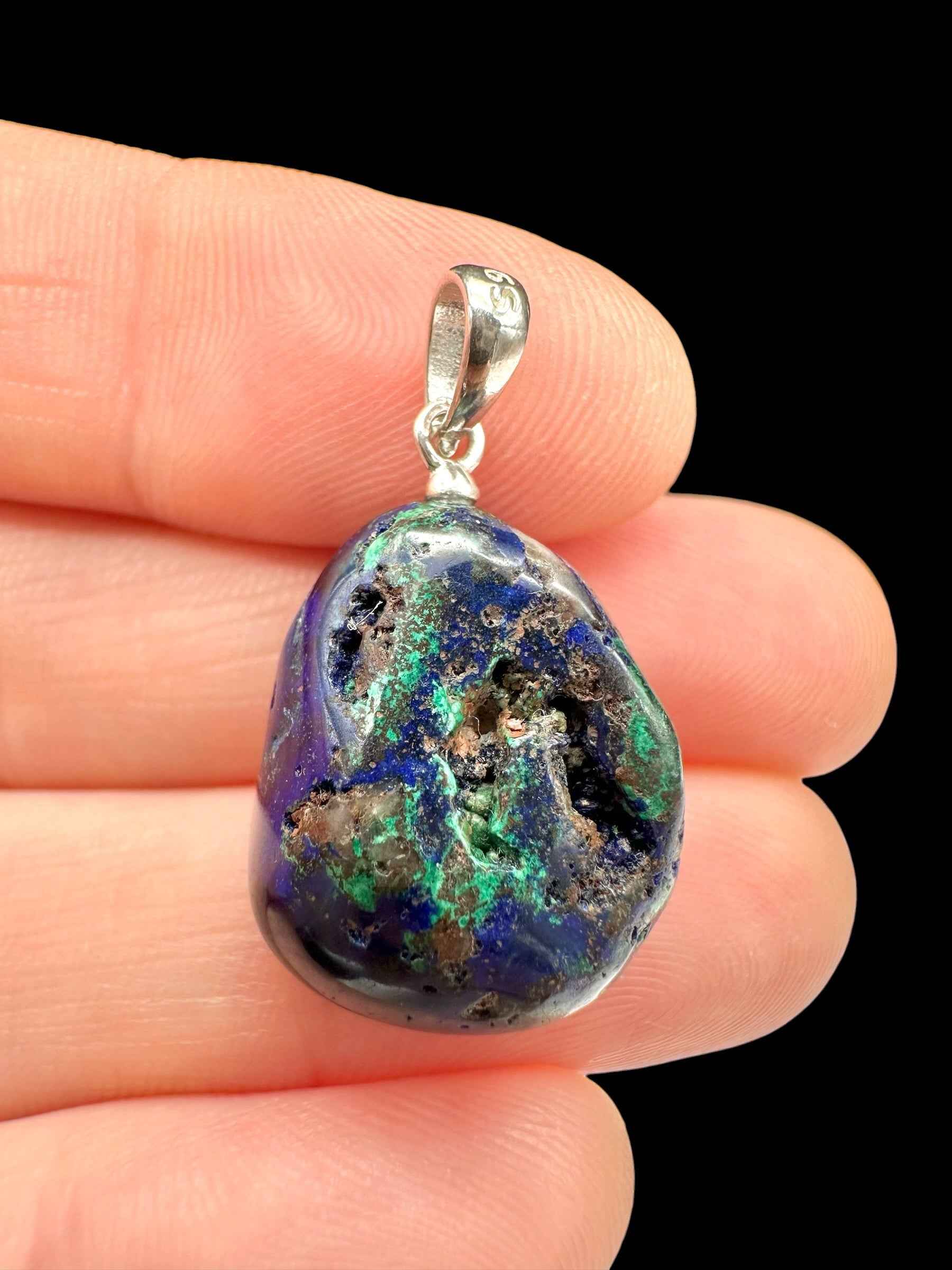 Pendente in azurite blu con chiazze di malachite verde, forma a goccia levigata, cappuccio in argento, tenuto tra le dita