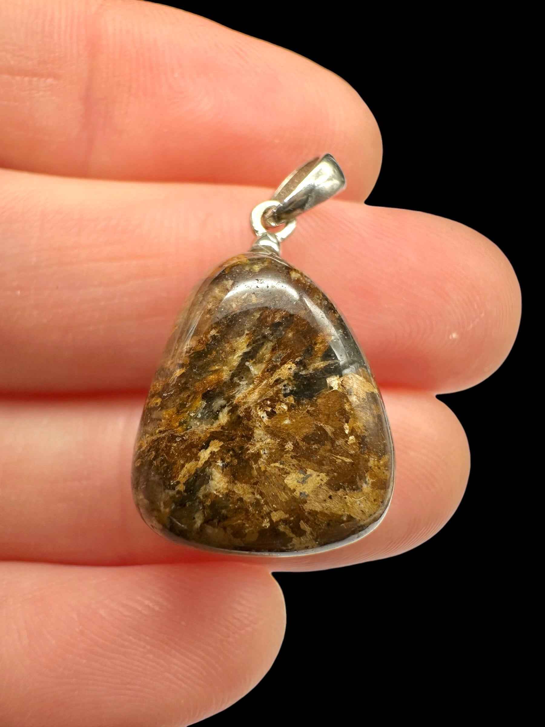 Pendente in bronzite a cabochon triangolare bruno con venature ocra, montatura in argento, tenuto tra le dita