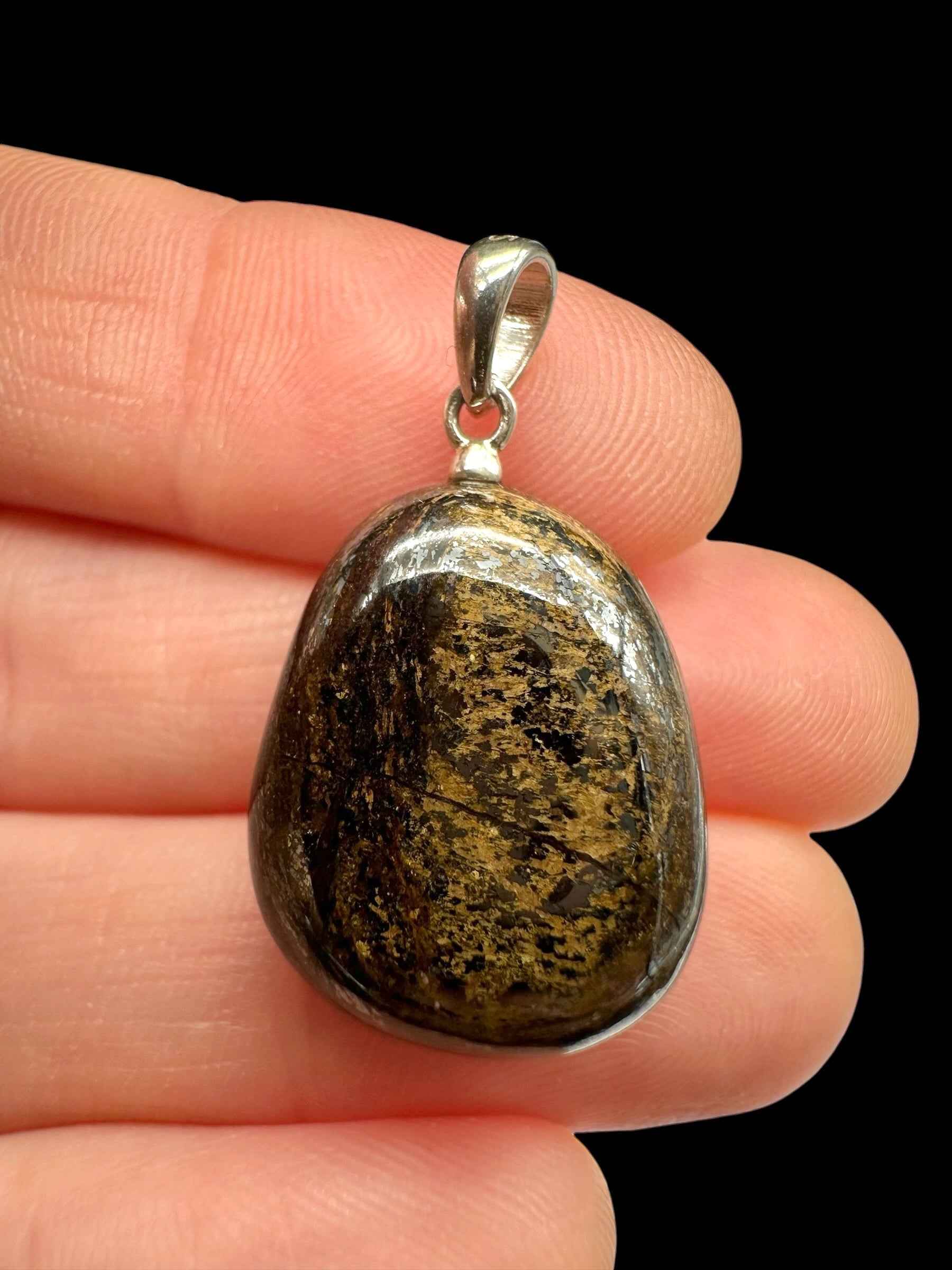 Pendente in bronzite bruna con chiazze dorate, cabochon a goccia montato in argento, tenuto tra le dita