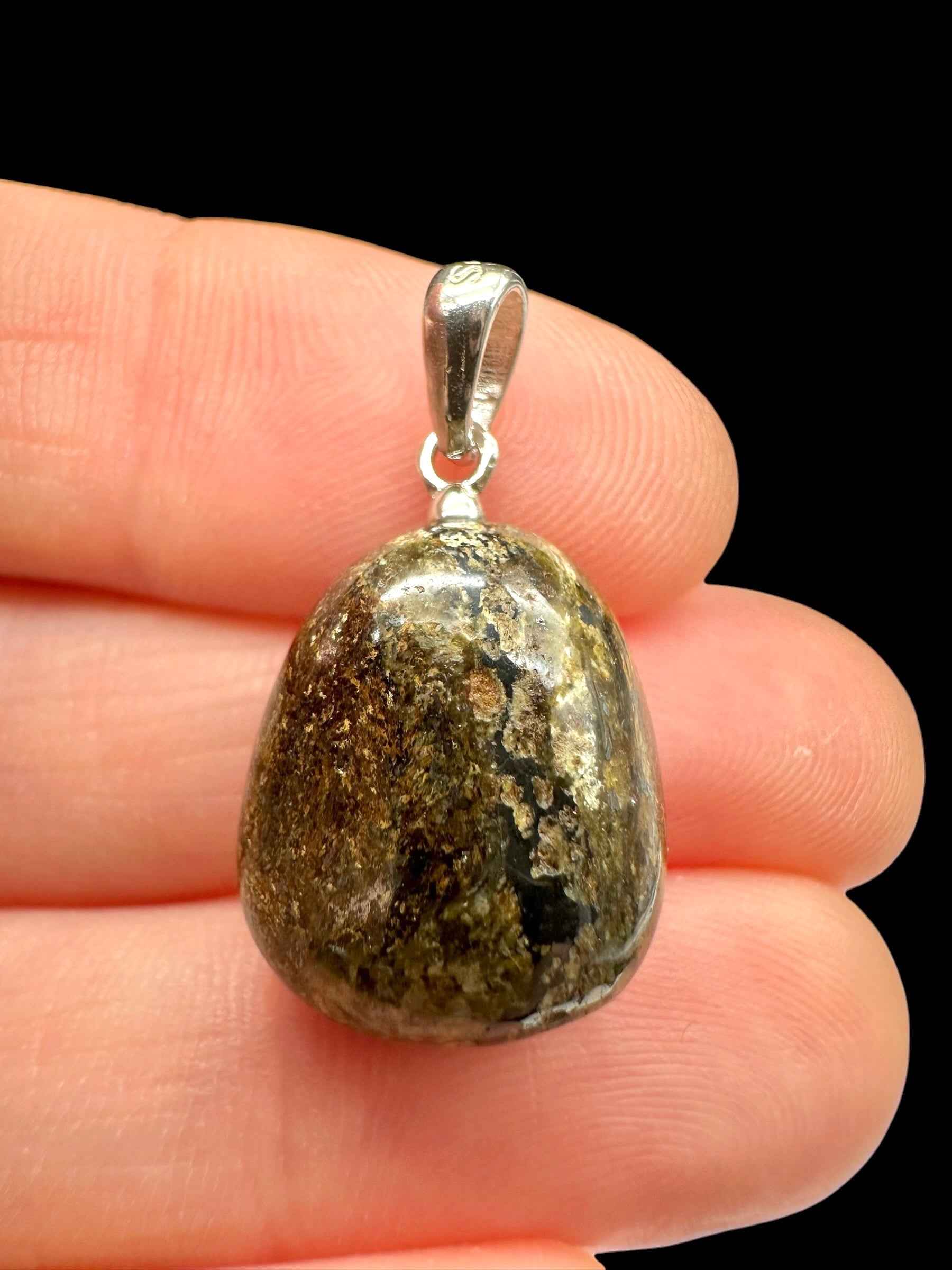 Pendente in bronzite a goccia levigata verde oliva e bruna con cappuccio in argento, tenuto tra le dita