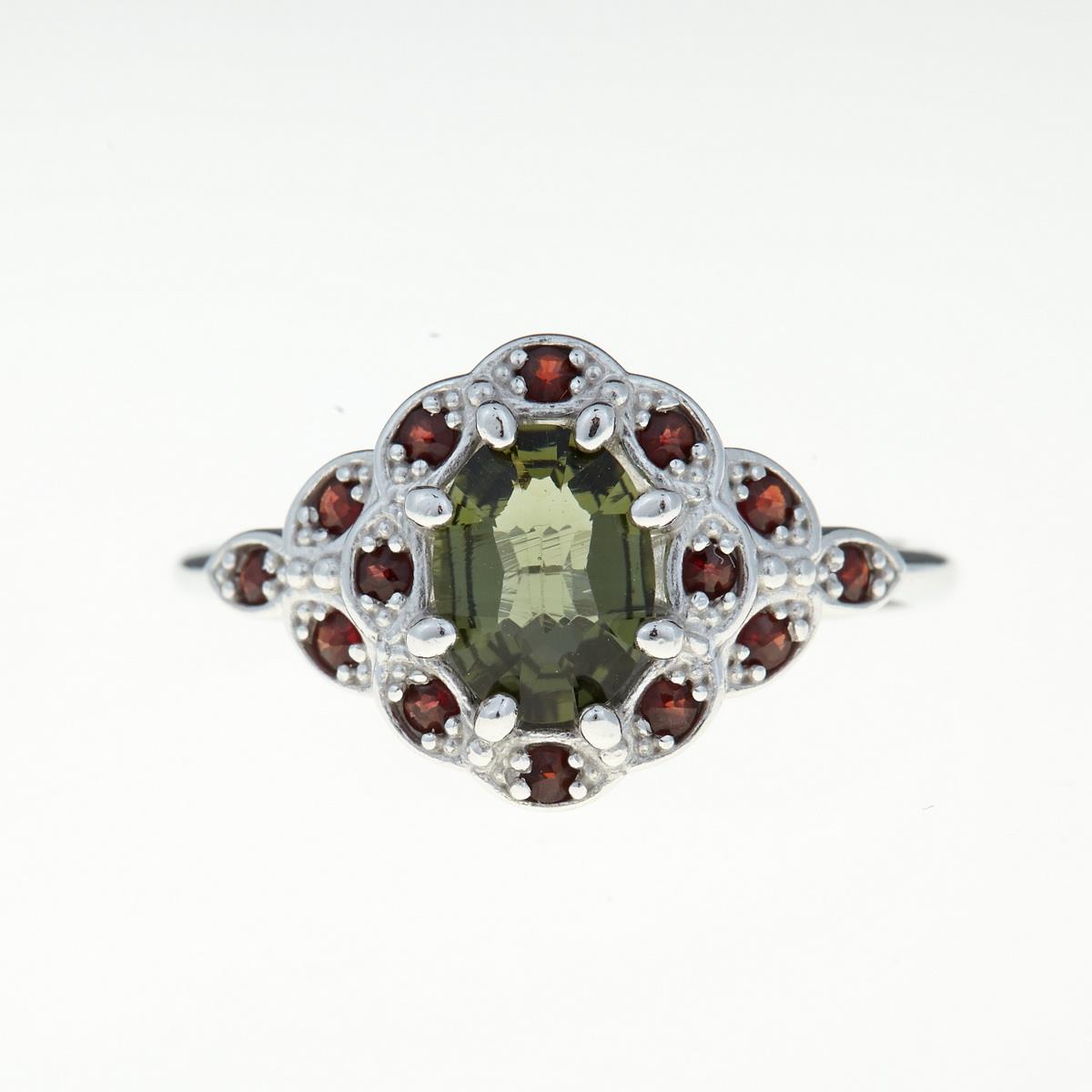 Anello in argento rodiato con moldavite faccettata ovale verde al centro e corona di granati rossi