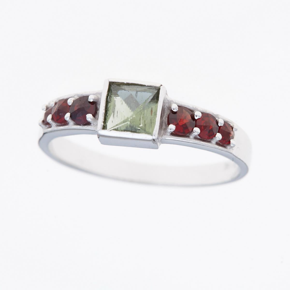 Anello in argento rodiato con moldavite verde quadrata al centro e sei granati rossi tondi sulle spalle
