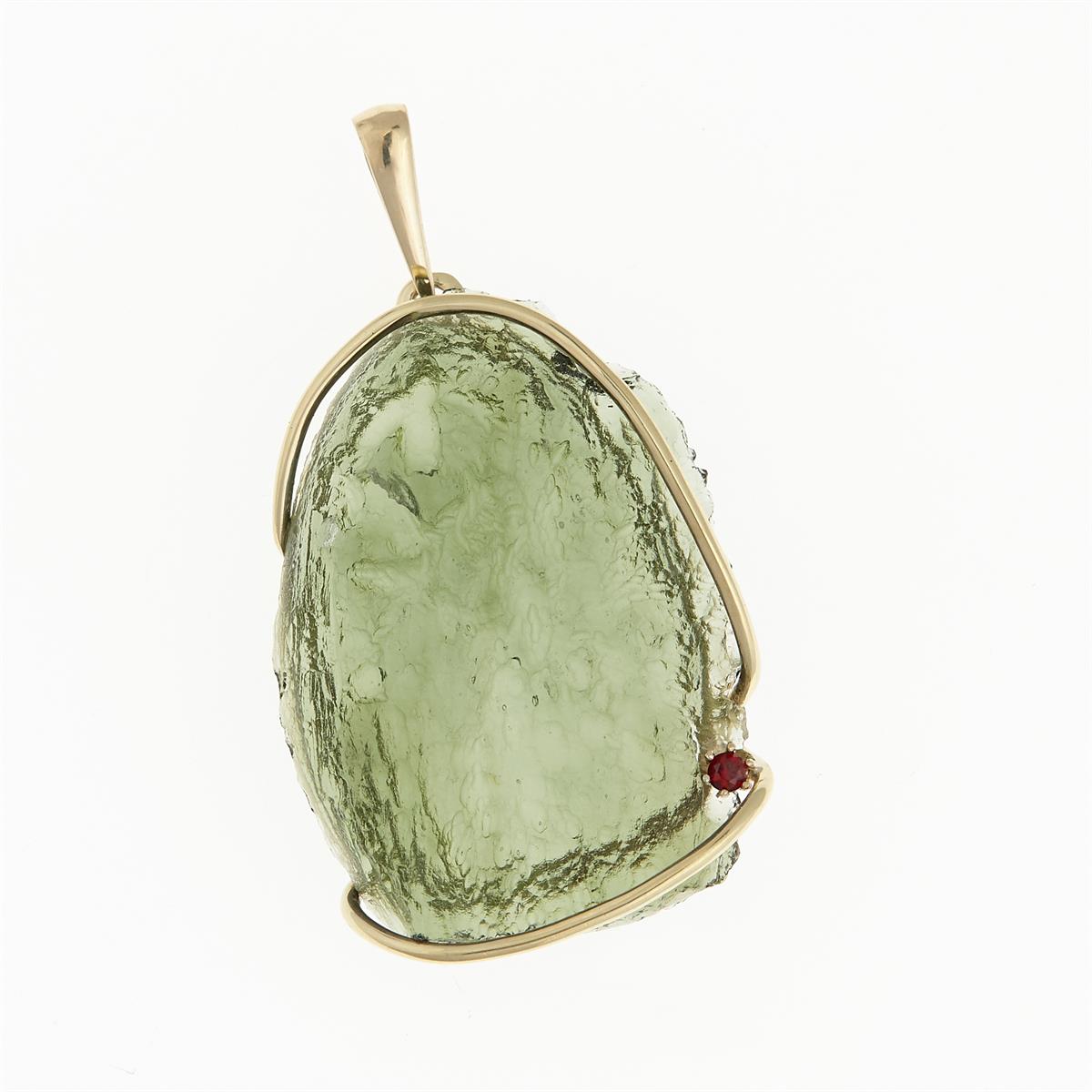 Pendente in oro giallo con moldavite grezza verde chiara a superficie rugosa e piccolo granato rosso